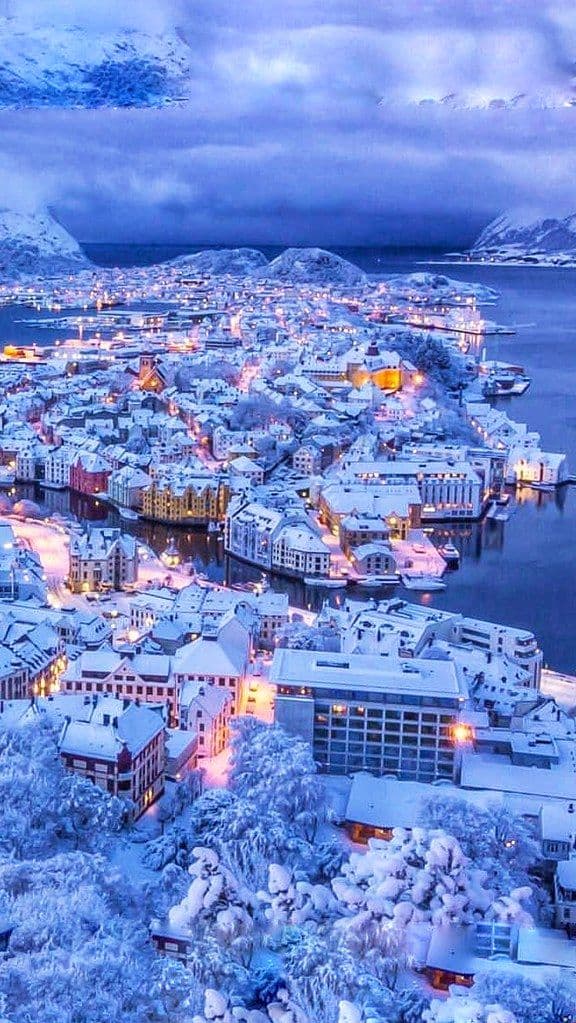 Snow-covered coastal city at blue hour with warm city lights.